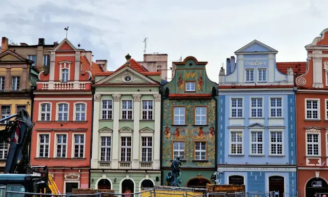 Färgglada husfasader i **Poznan, Polen**, med detaljerade ornament och tak. En byggkran syns i förgrunden.