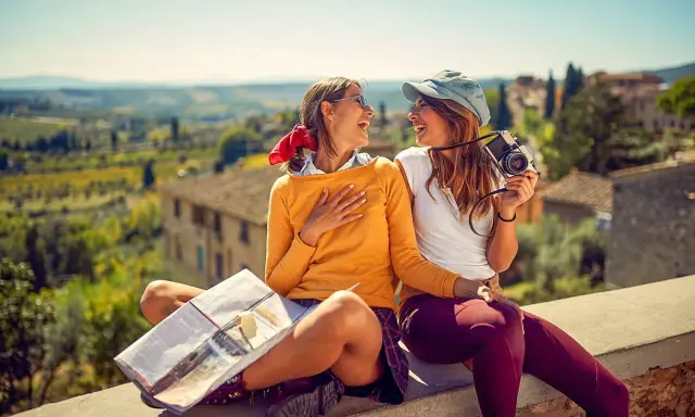 Två glada vänner njuter av sin resa i Europa, med en karta och kamera redo för nya äventyr i en vacker italiensk landskapsvy.