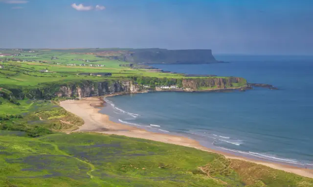 Grönskande kullar och en sandstrand vid havet på Irland, nära Belfast.