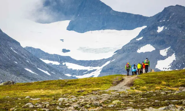 Vandringsgrupp på väg uppför en stenbelagd stig mot Sylarnas glaciärklädda toppar.