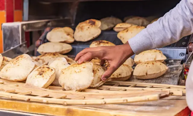 En hand tar färskt, fluffigt bröd från en ugn. Detta är en del av den autentiska egyptiska maten, perfekt för att doppa i läckra röror.