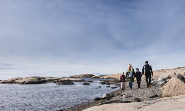 Familj promenerar längs en stenig strand vid Tjurpannans naturreservat.