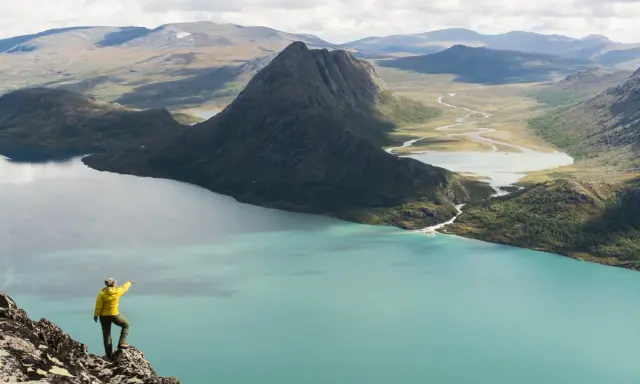 Vandrare pekar ut över turkost vatten och berg under en Besseggen vandring.