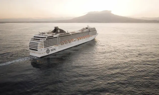 Kryssningsfartyget MSC Poesia glider fram på havet i solnedgången, med en vulkan i bakgrunden.