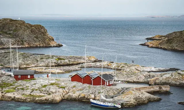 Röda sjöbodar och segelbåtar på klippor vid havet. En idyllisk bild av sommar i Sverige.