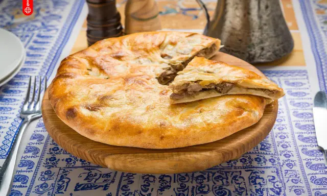 En gyllene, nybakad khachapuri, en klassisk georgisk mat, ligger på en träskärbräda. En bit är uppskuren och visar det smakrika köttfyllningen.