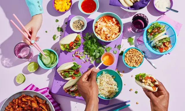 En festlig dukning med asiatiska frukter och bao buns. Färgglada skålar med mango, kimchi, jordnötter och grönsaker.