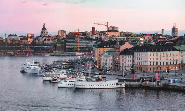 Stockholms silhuett med fartyg i hamnen vid solnedgången. En perfekt vy för att uppleva Stockholm.