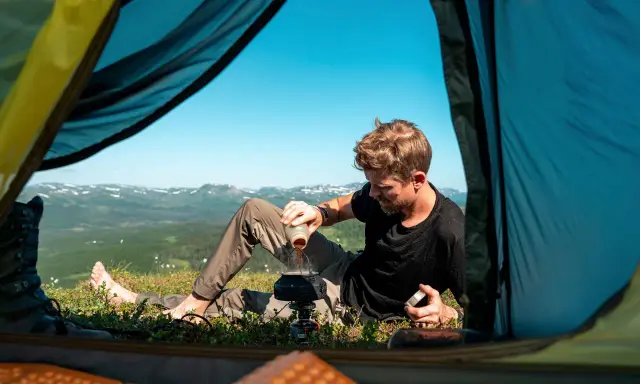 Man gör kaffe vid tältöppningen under en vandring i Sverige sommar. Vacker utsikt över fjällen.