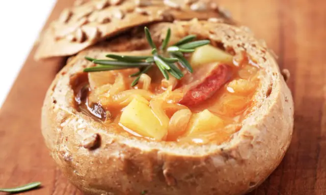 En mustig gryta med potatis och korv serveras i ett urgröpt bröd, en härlig tjeckisk matupplevelse.