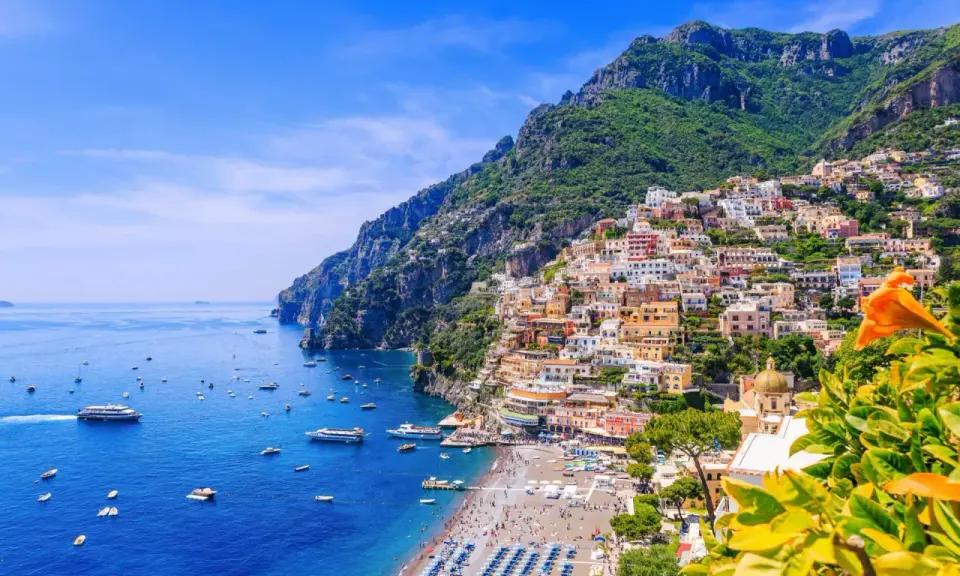 Färgglada hus klättrar uppför bergssluttningen vid en livlig strand och blått hav. En vacker vy som ger fakta om Italien.