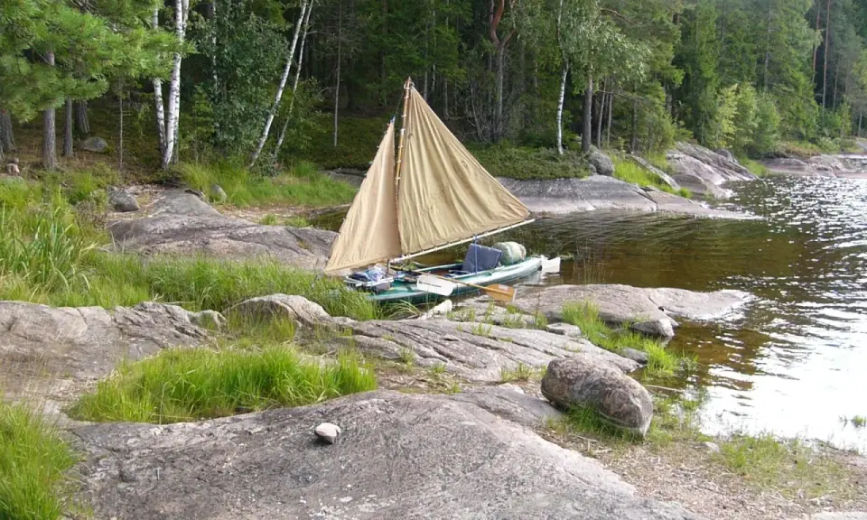 En liten segelbåt med åror ligger vid en stenig strand. En härlig plats att paddla Dalslands kanal på.