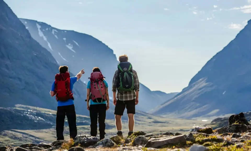 Två vandrare med ryggsäckar blickar ut över en dal under en kungsleden vandring. En pekar mot bergen.