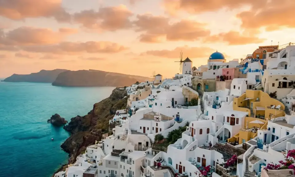 Vacker solnedgång över Oia, Santorini. Vita hus klättrar längs klippan ner mot det turkosblå havet. En dröm om en resa till Grekland.