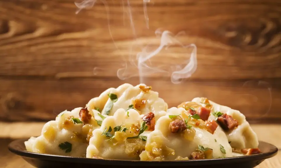 Ångande pierogi, en klassisk polsk mat, serveras på en mörk tallrik med lök och persilja.