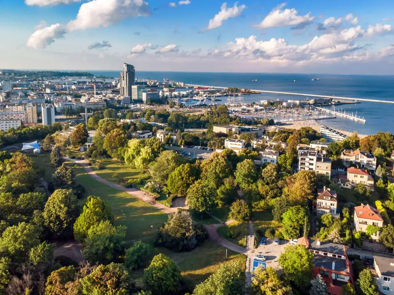 Vacker utsikt över Gdynia, Polen, med en grönskande park i förgrunden och en livlig hamn vid Östersjön.