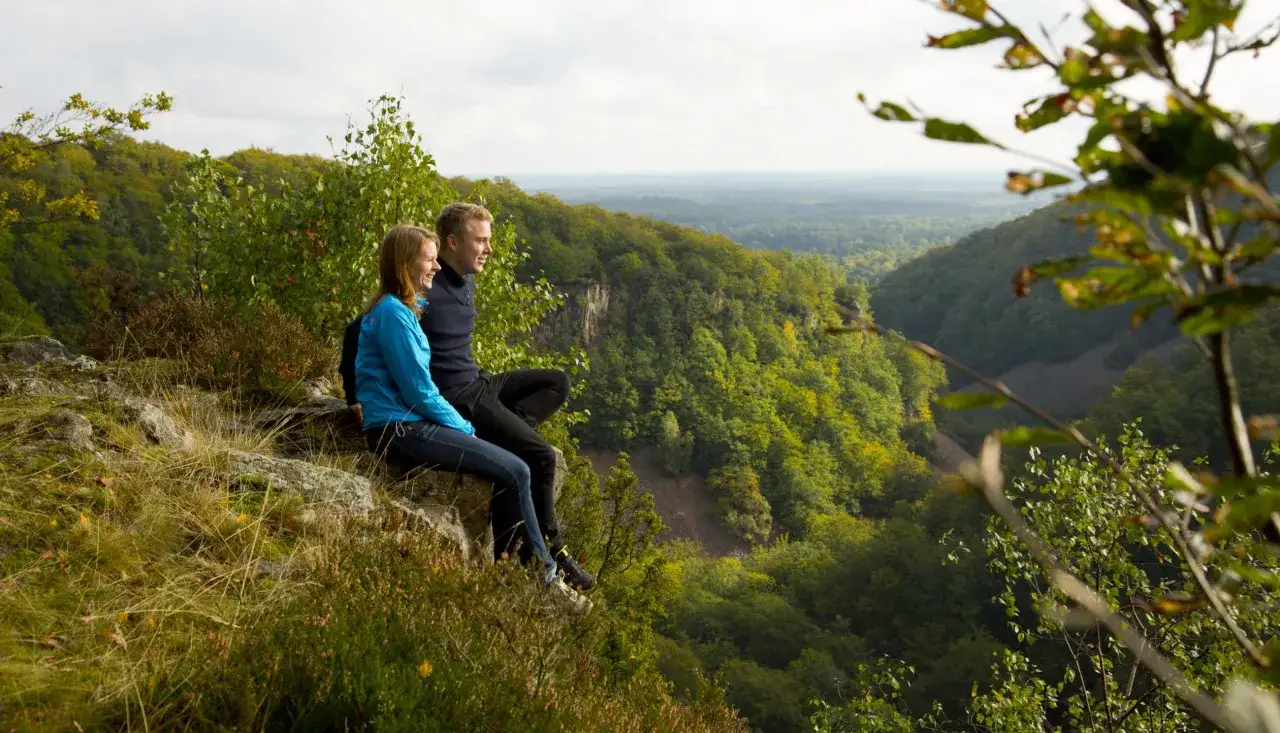 Ett par njuter av utsikten över en grönskande dal i Skåne. Perfekt för aktiviteter Skåne vuxna som vandring och naturupplevelser.
