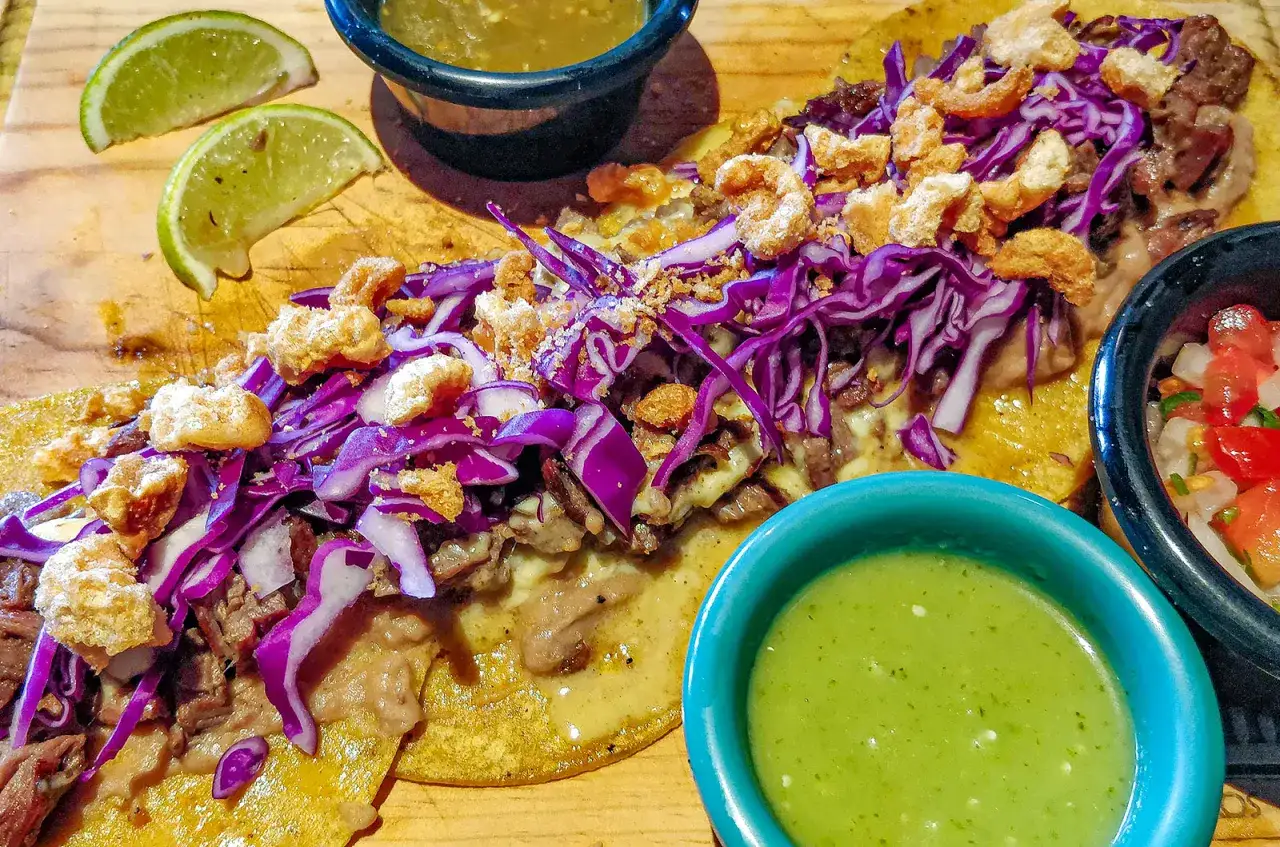 En smak av mexiko mat: en taco med kött, rödkål och krispiga bitar, serverad med lime och två sorters salsa.