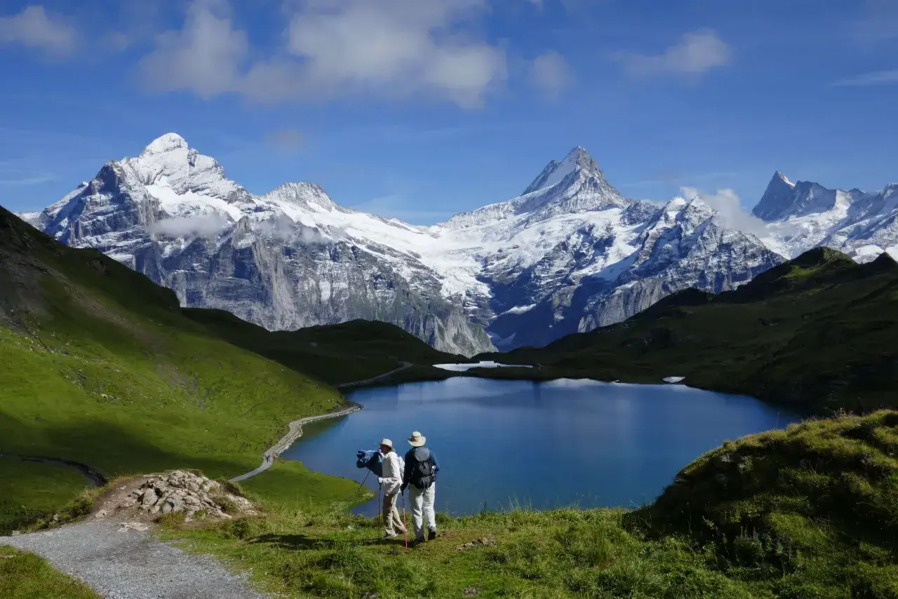 Två vandrare njuter av en fantastisk vy över en blå sjö och snöklädda berg under en vandring i Schweiz.