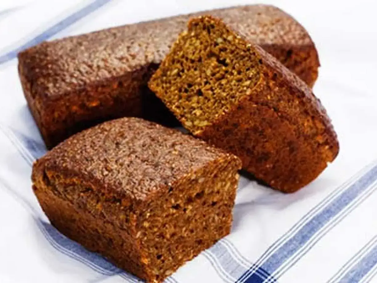 Tre mörka, saftiga rågbröd ligger på en randig duk. Perfekt för en äkta dansk mat-upplevelse.