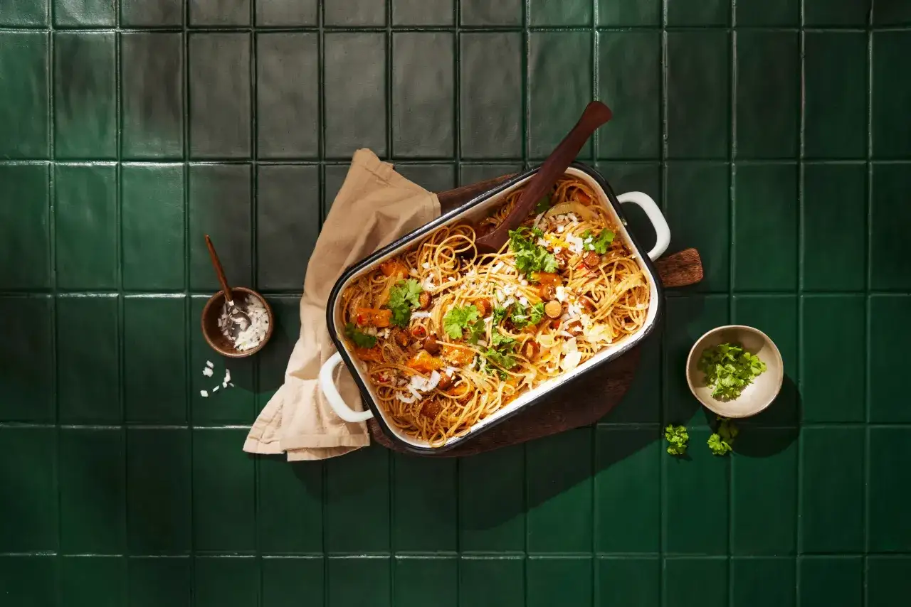 En stor ugnsform med spaghetti, pumpa och korv, perfekt för ett gott pastitio recept. Garnerad med färsk persilja och lök.
