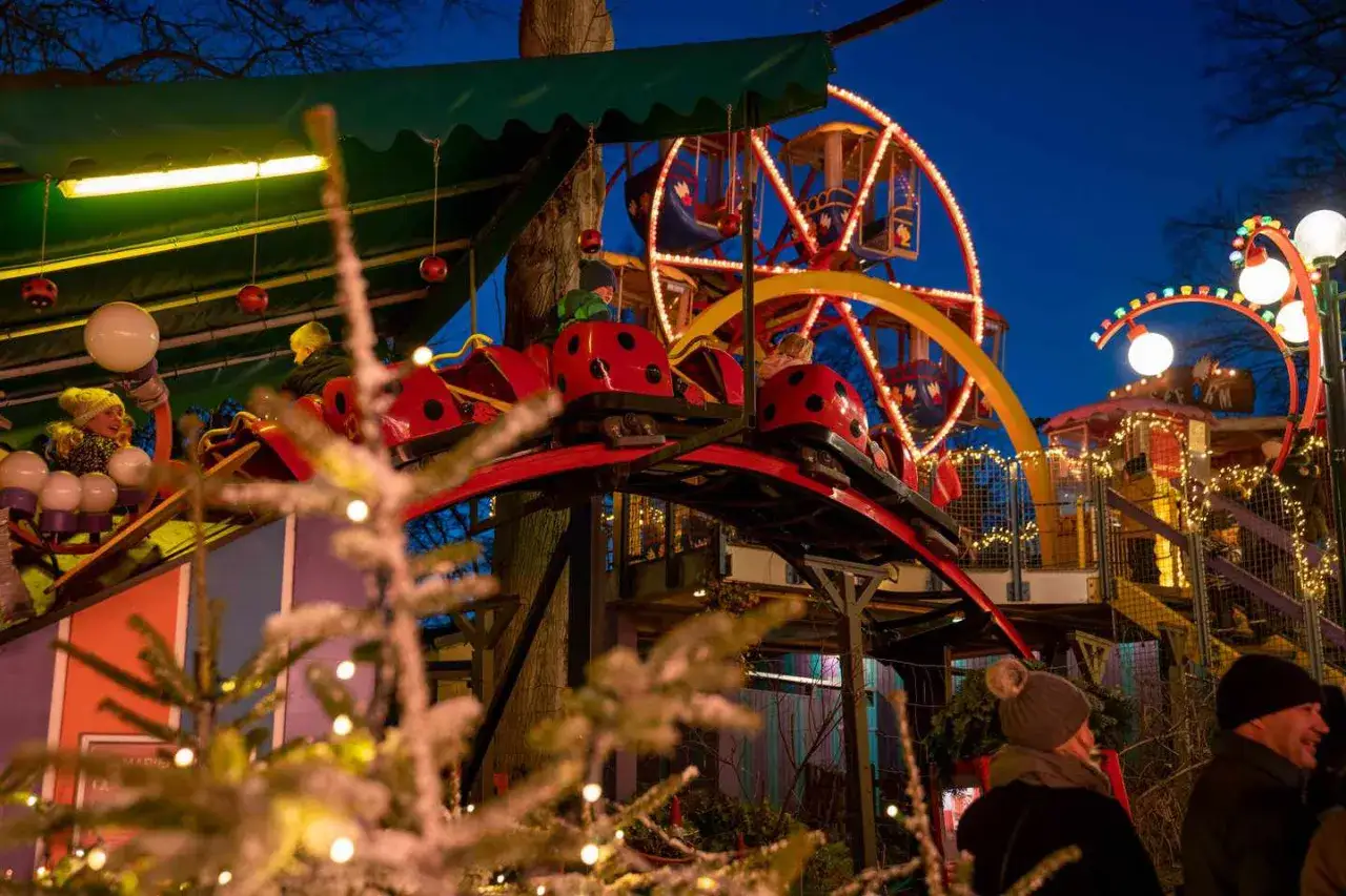 Barn njuter av en åktur på en nyckelpiga-berg-och-dalbana på en julmarknad. Ett par i förgrunden ler.