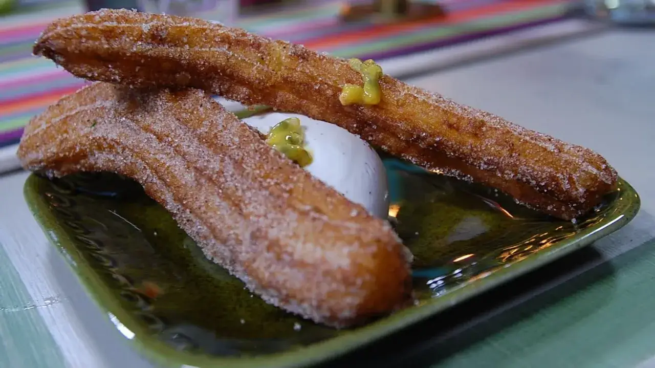 Tv&aring; sockerstr&ouml;sslade churros, friterad deg, ligger p&aring; en gr&ouml;n tallrik med en kula vaniljglass och passionsfruktss&aring;s.