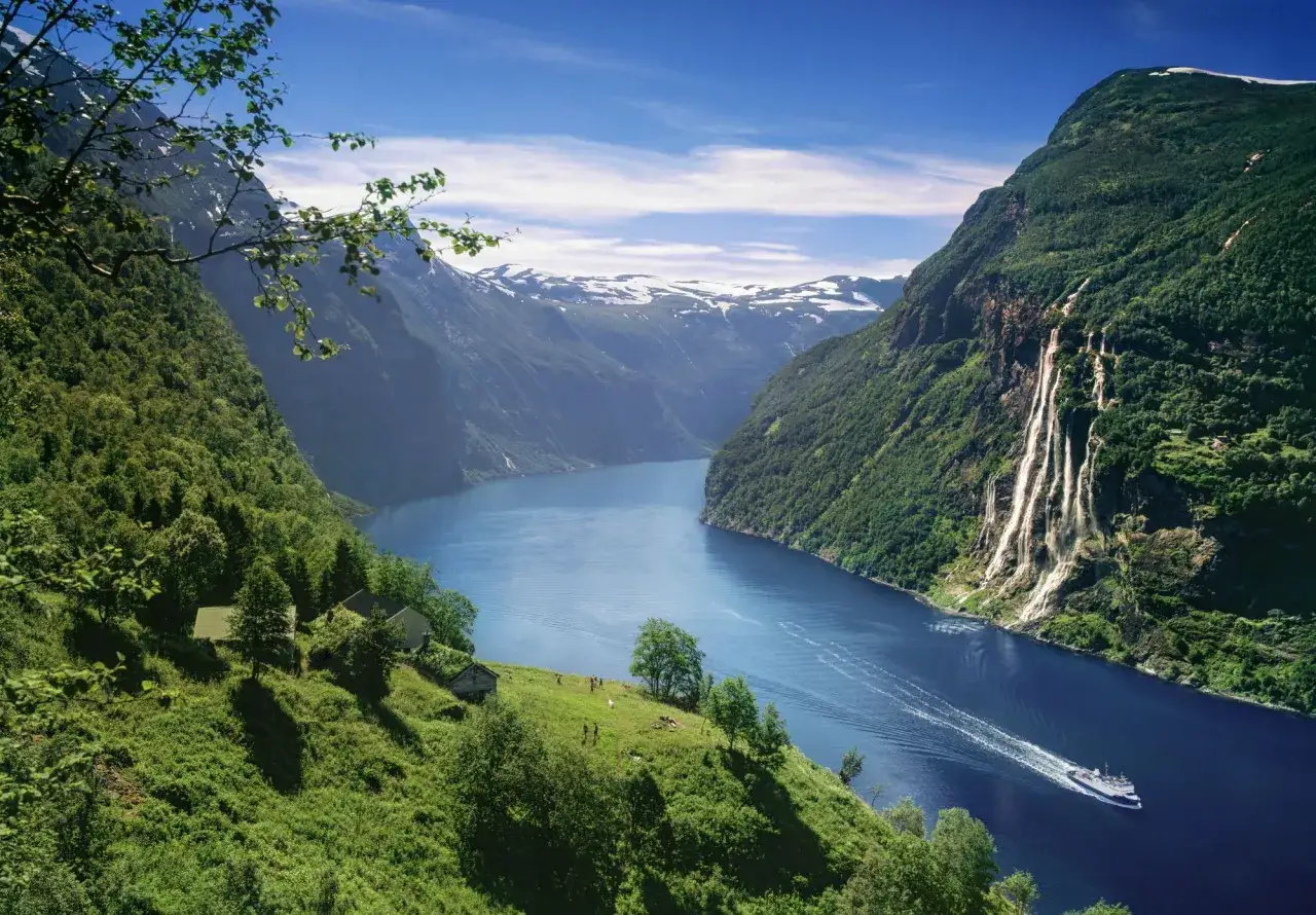 En båt färdas på en djupblå fjord omgiven av gröna berg med vattenfall. En idyllisk plats för oförglömliga upplevelser i Norge.