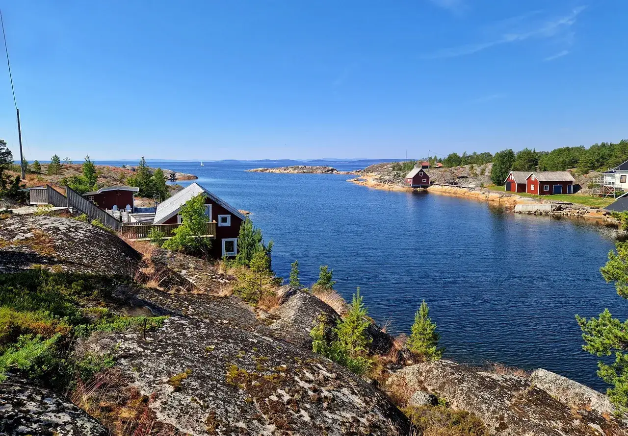 Röda stugor vid en blå vik, omgivna av klippor och träd. En idyllisk vy som kan vara sveriges finaste strand.