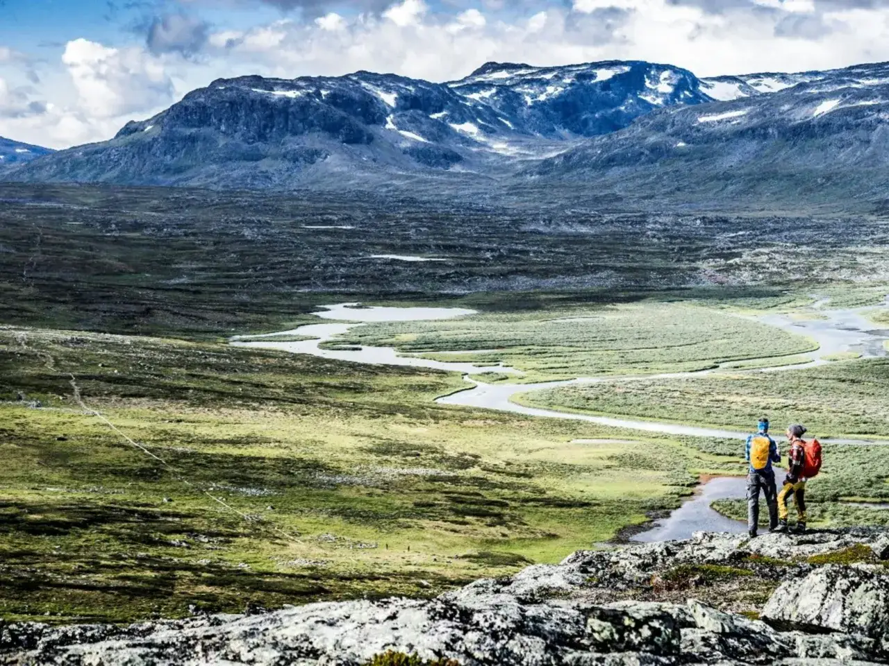Två vandrare njuter av utsikten över ett vidsträckt landskap med en slingrande flod, en perfekt plats för kungsleden vandring.