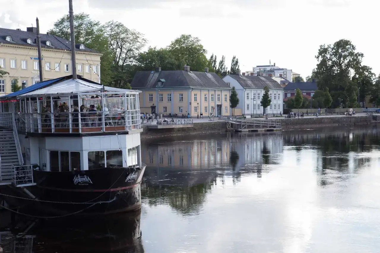 En båt med restaurang ligger vid kajen i Karlstad. Vackra gamla hus speglar sig i vattnet, en fin plats att se i Karlstad.