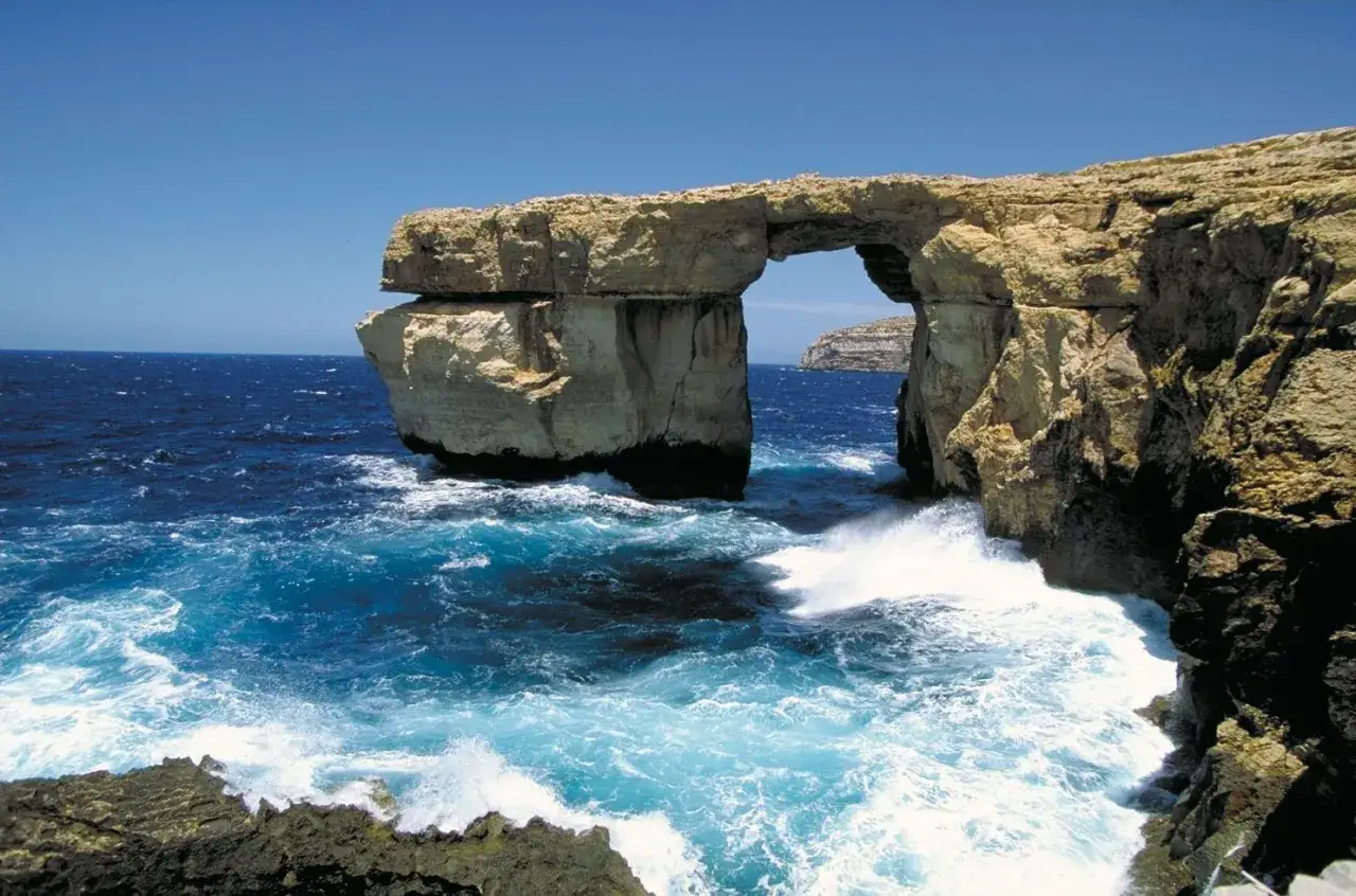Blå havsvågor slår mot klippor och en imponerande stenbåge på Malta. En vy av malta natur.