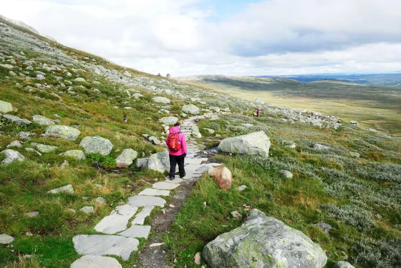 Vandrare med röd ryggsäck på stenlagd stig i fjällandskap. En klassisk Fjällräven-upplevelse.