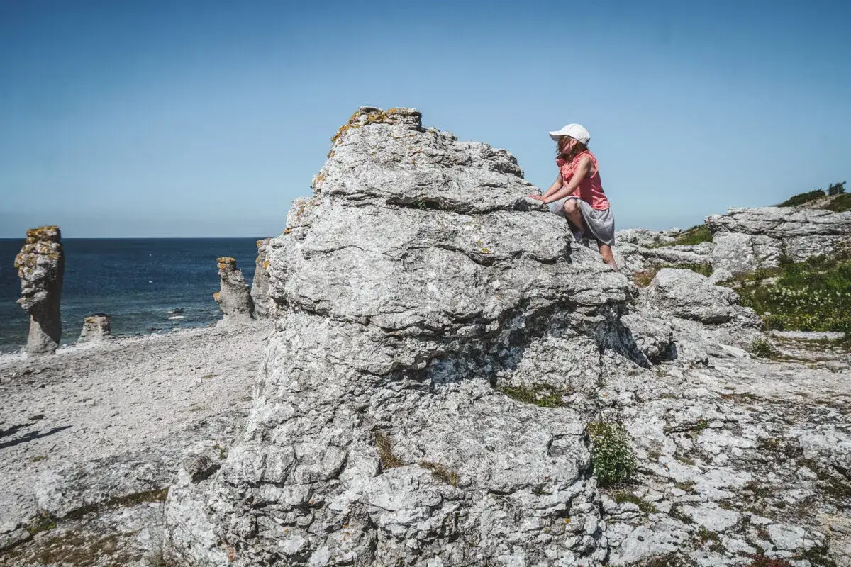 Barn utforskar raukar på Gotland. En flicka klättrar på en stenformation vid havet.
