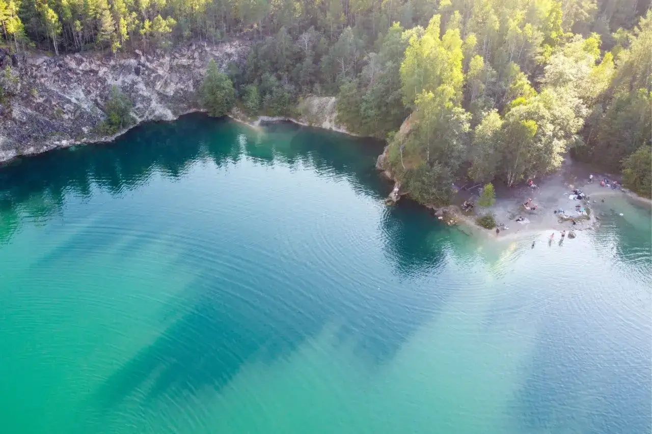 Turkost vatten i ett gammalt kalkbrott nära Stockholm, med människor som solar och badar på stranden.