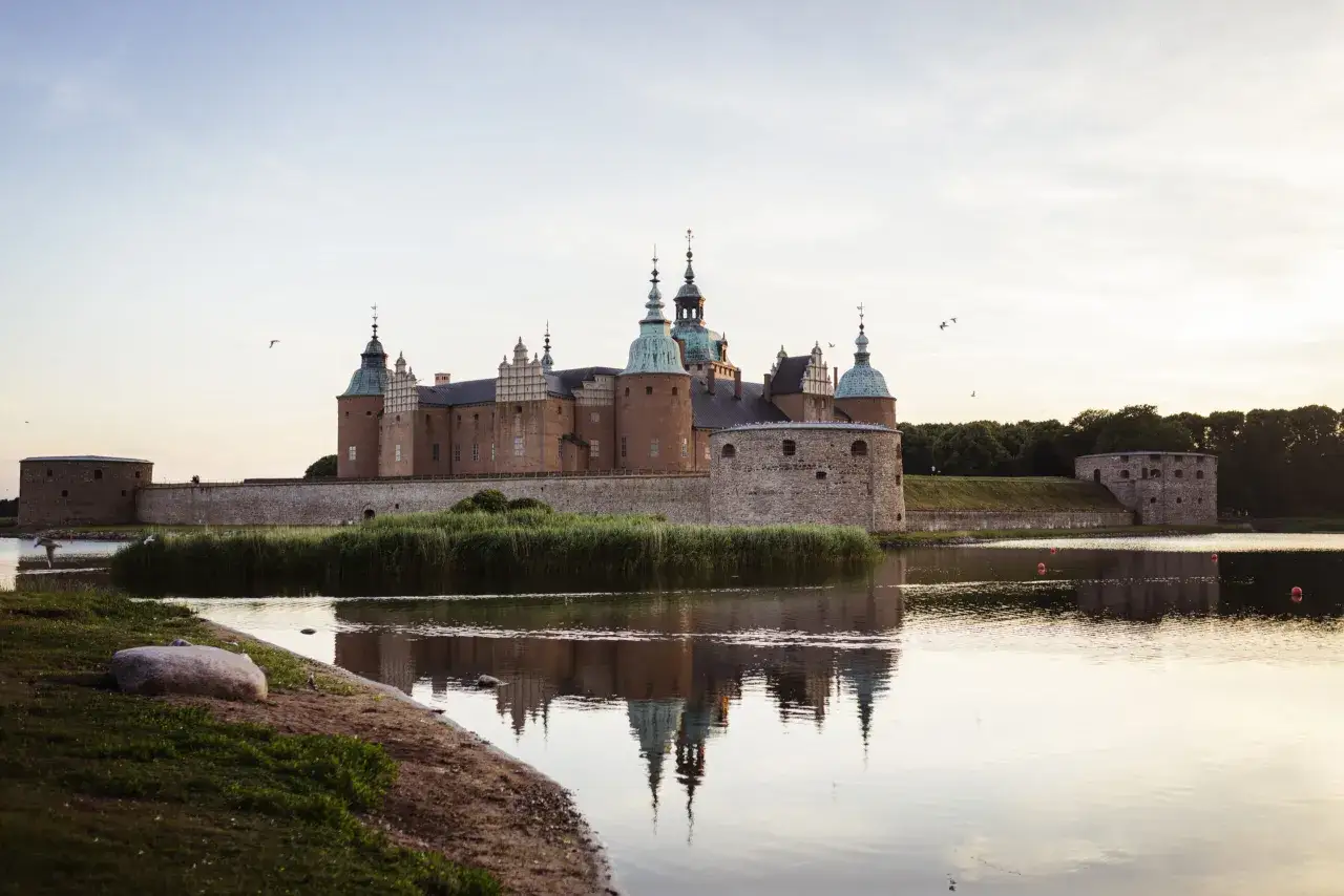 Kalmar slott speglar sig i vattnet vid solnedgången. En vacker plats för upplevelser i Kalmar.