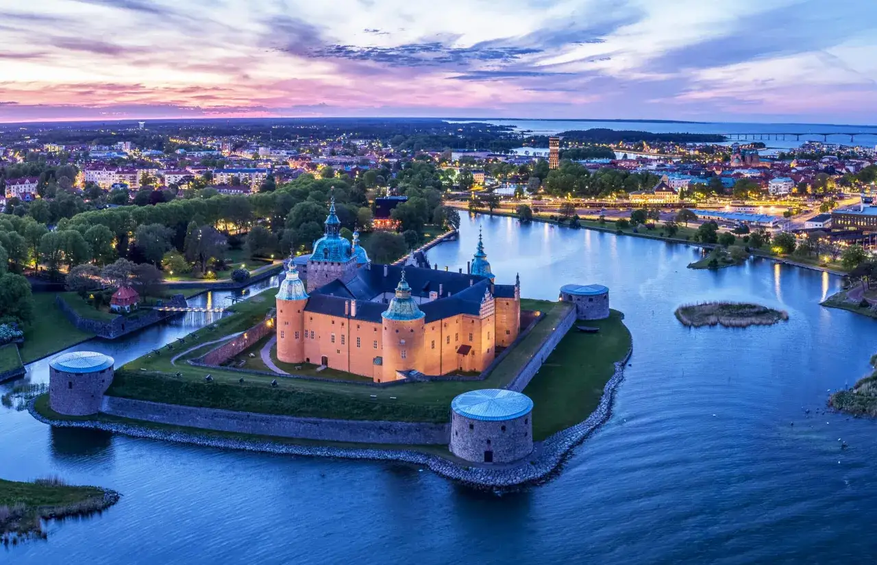 Kalmar slott badar i kvällsljus, en del av oförglömliga upplevelser i Kalmar. Staden vaknar till liv med ljus längs vattnet.
