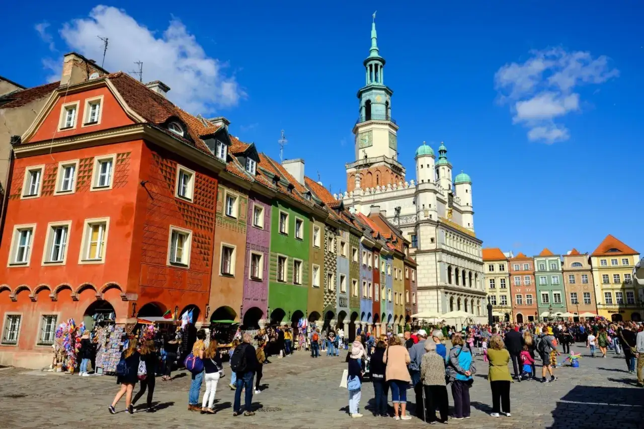 Färgglada hus på ett torg i Poznan, Polen. Människor promenerar och njuter av solen.