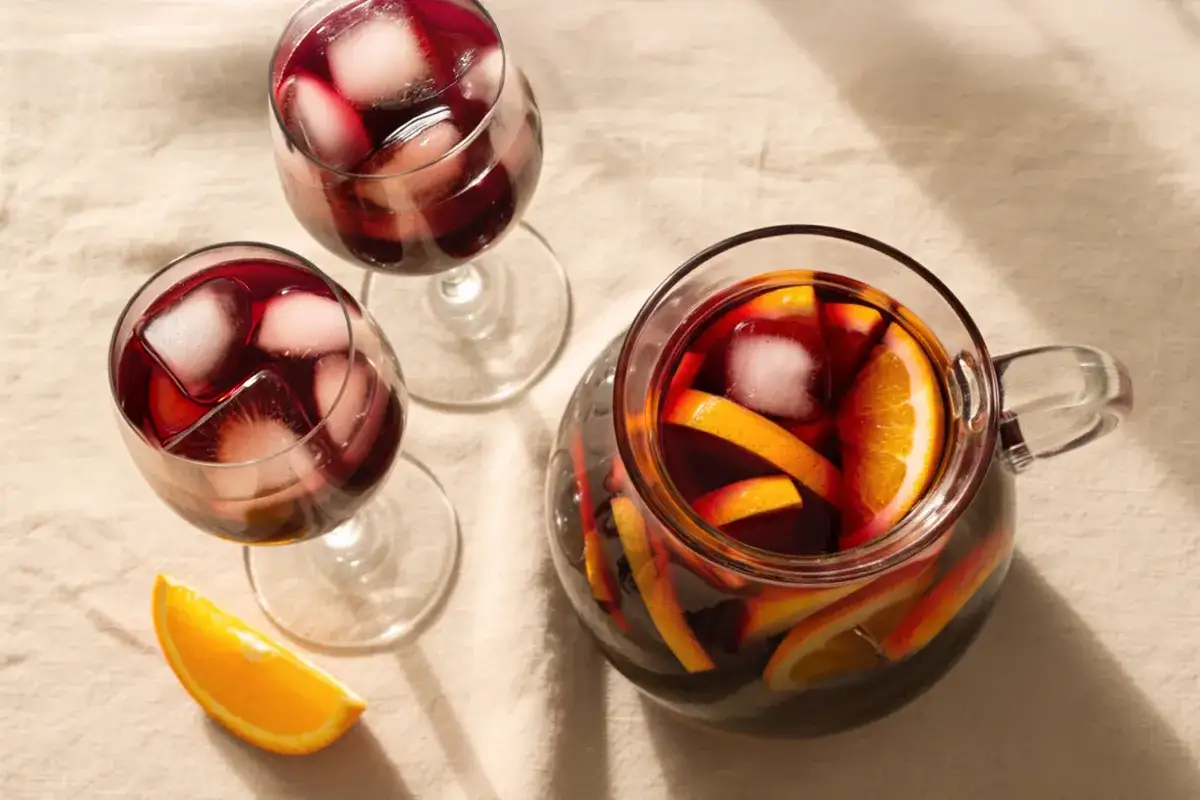 Sangria recept original: en karaff och två glas fyllda med röd sangria, is och apelsinskivor.