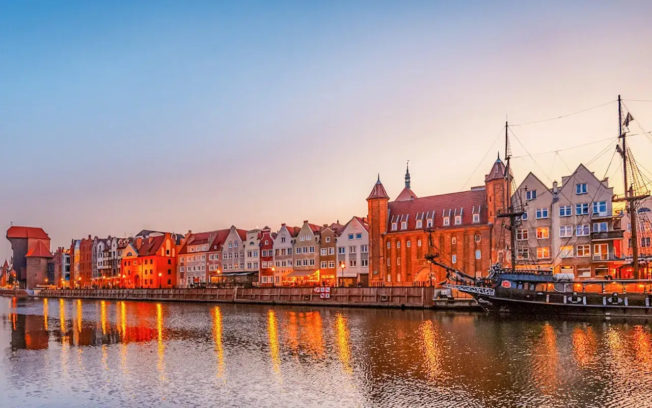 Färgglada hus längs floden i Polen, Gdansk, med en gammal träbåt som ligger vid kajen.