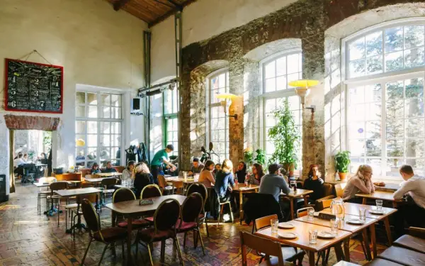 Folk äter och dricker på en livlig restaurang i Tallinn. Stora fönster släpper in solljus i lokalen med rustika tegelväggar.