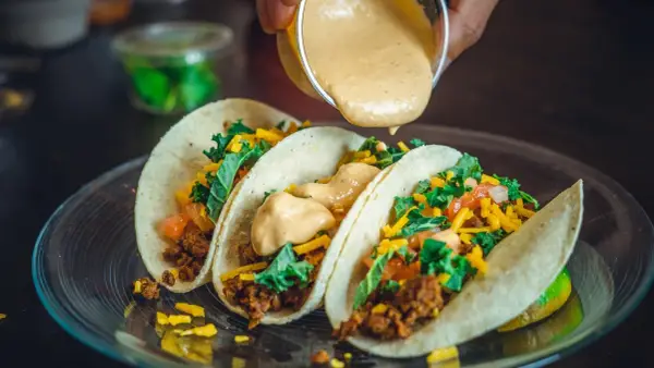 Tre läckra tacos med köttfärs, grönsaker och ost. En krämig sås hälls över dem, perfekt mexikansk mat.