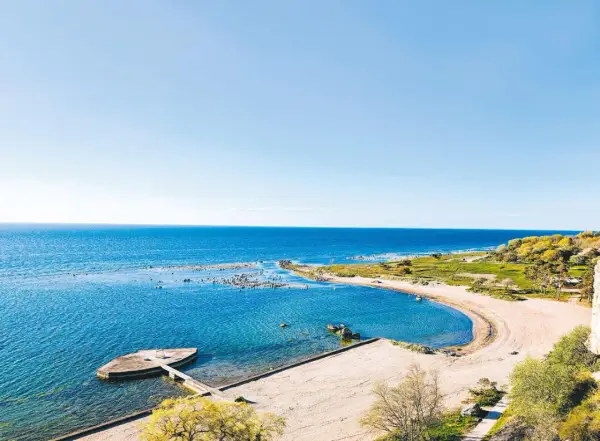 En vacker vy över ett vattenland på Gotland med en sandstrand, klart blått hav och gröna kullar.