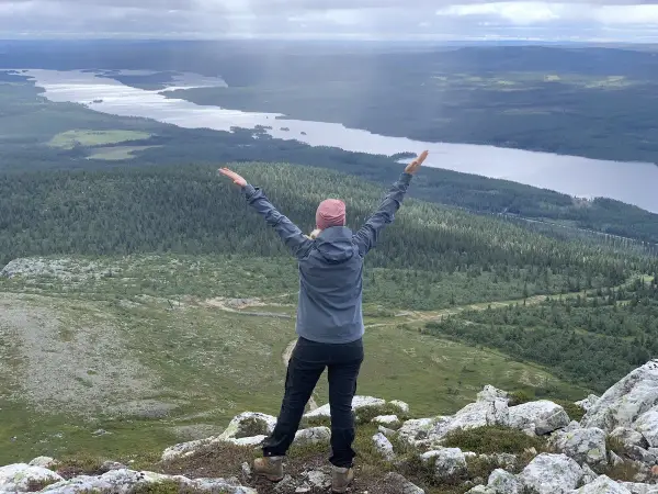 En person med armarna uppsträckta njuter av en fantastisk utsikt över sjöar och skogar under en Lofsdalen vandring.