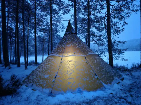 Varmt ljus lyser från ett snötäckt tält i Glaskogens naturreservat. En magisk vinterkväll.