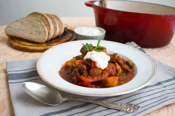 En portion mustig ungersk mat, en mustig gryta med kött och grönsaker, toppad med gräddfil och persilja. Serveras med gott bröd.