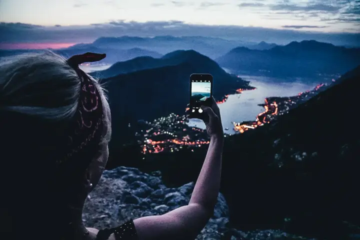 En person tar bild med mobiltelefonen av en stad vid havet i skymningen. En perfekt vy under en bilsemester Europa.