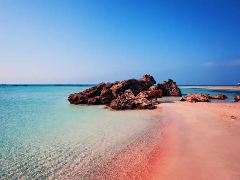 En rosa strand på Kreta med turkost vatten och klippor. En dröm för alla som älskar en kreta rosa strand.